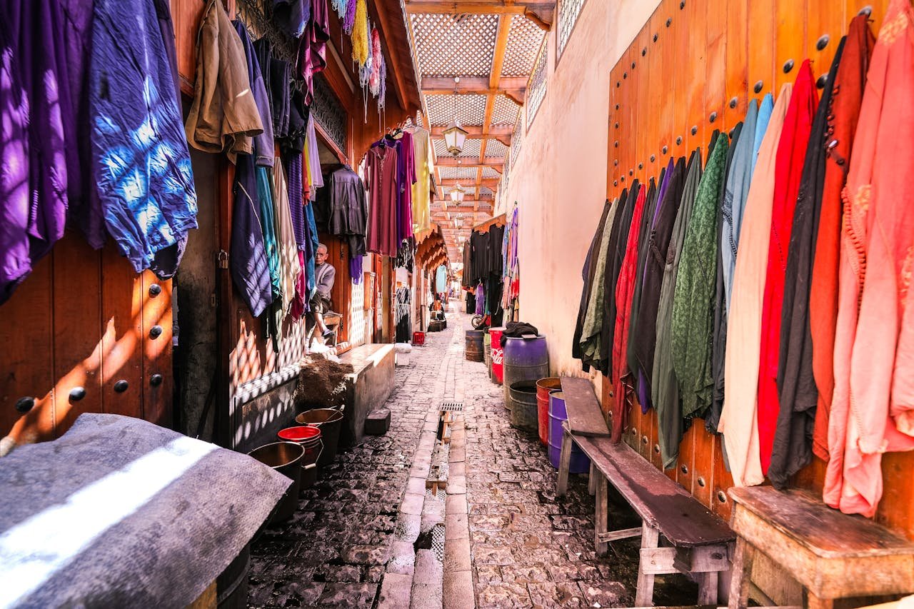 Colorful clothing hung in a sunny market alley, showcasing vibrant fabrics for sale.